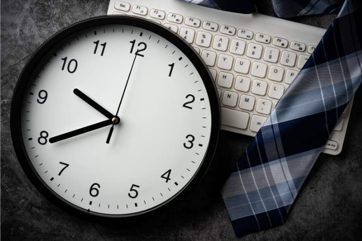Relógio de ponto e calendário sobre mesa de escritório ao lado de calculadora, simbolizando cálculo de horas extras trabalhistas, fotografia realista