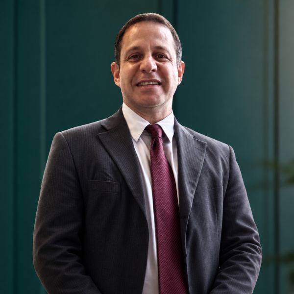 Retrato profissional de Dr. Alexander Nogueira, advogado trabalhista sênior, terno escuro, sorrindo, fundo neutro, fotografia corporativa realista